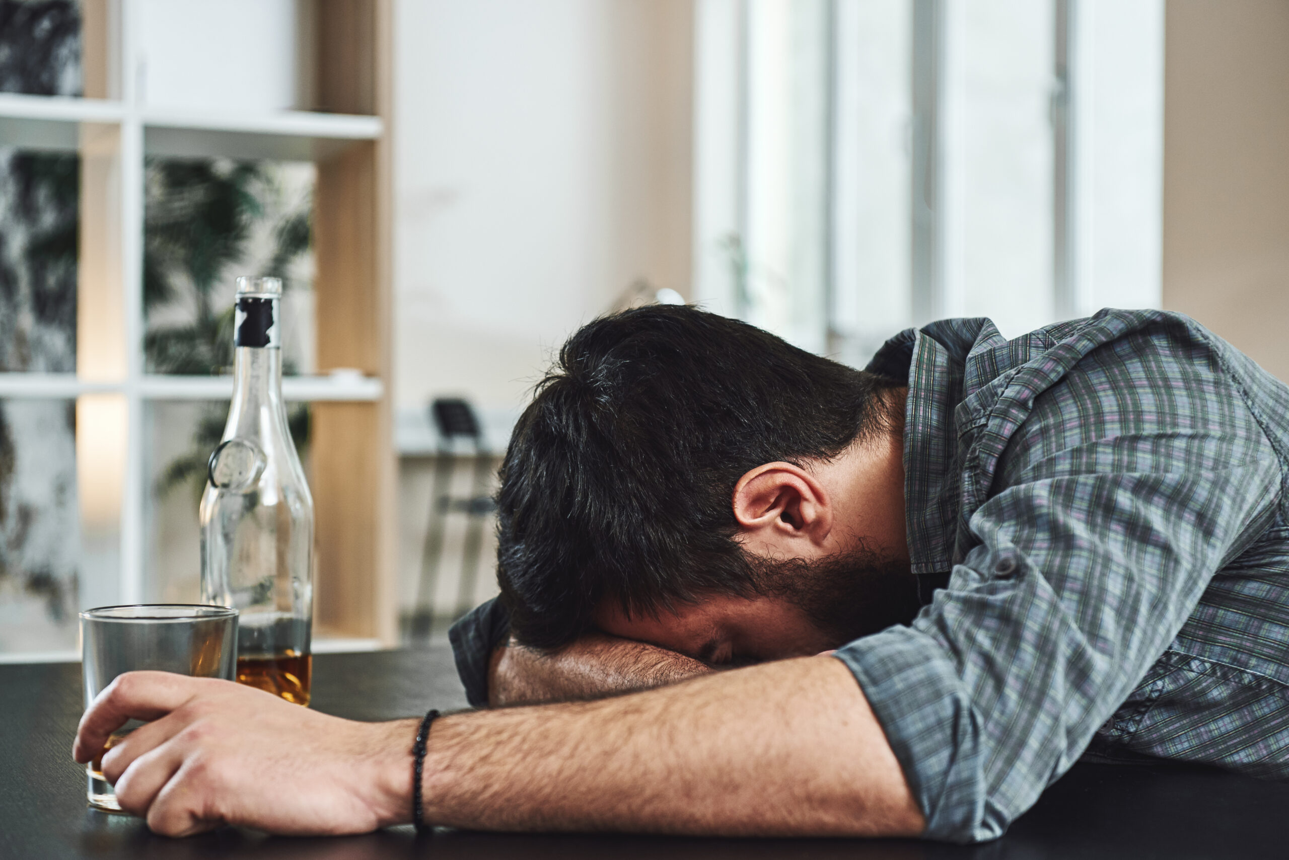 A man with his head down while holding a glass of alcohol for the topic gray area drinking.