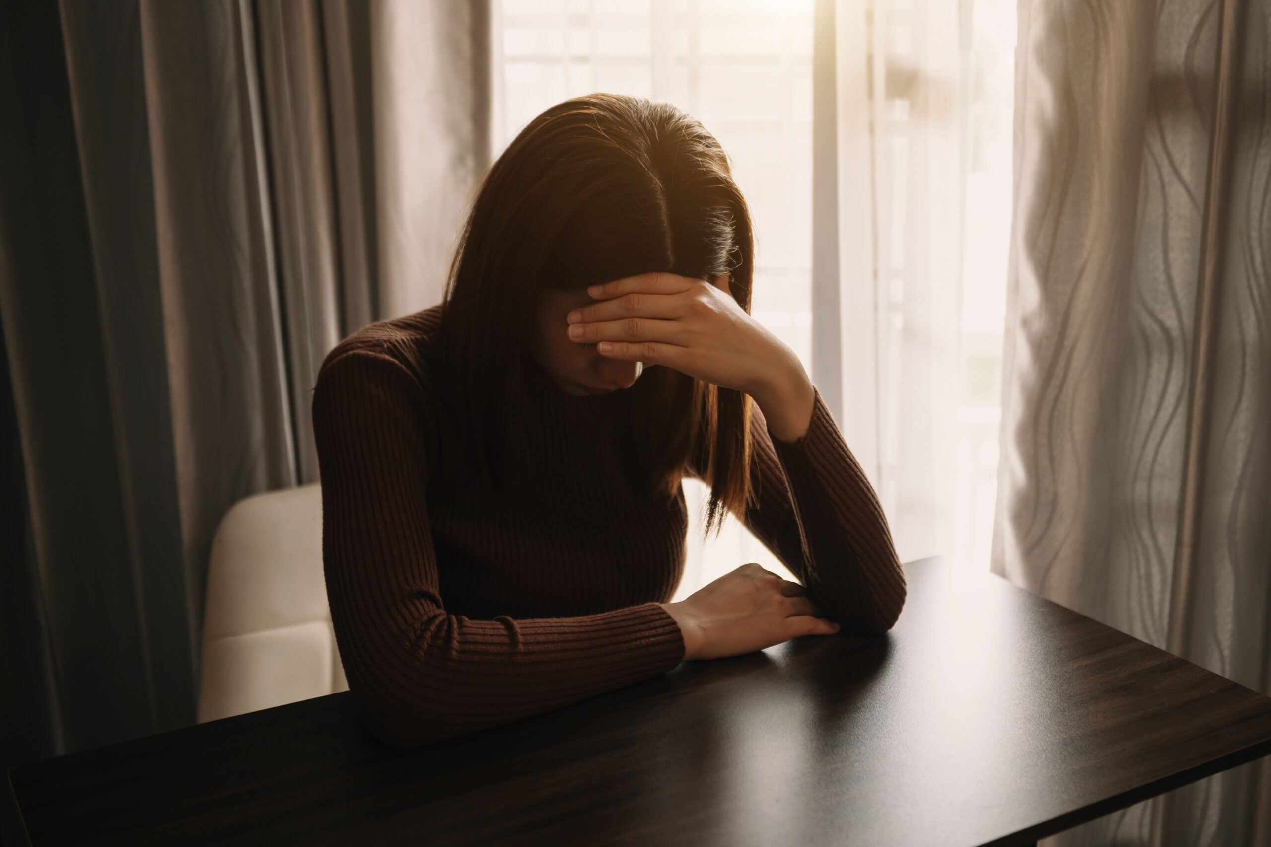 A woman going through kratom withdrawal sitting at a table with her head in her hands.