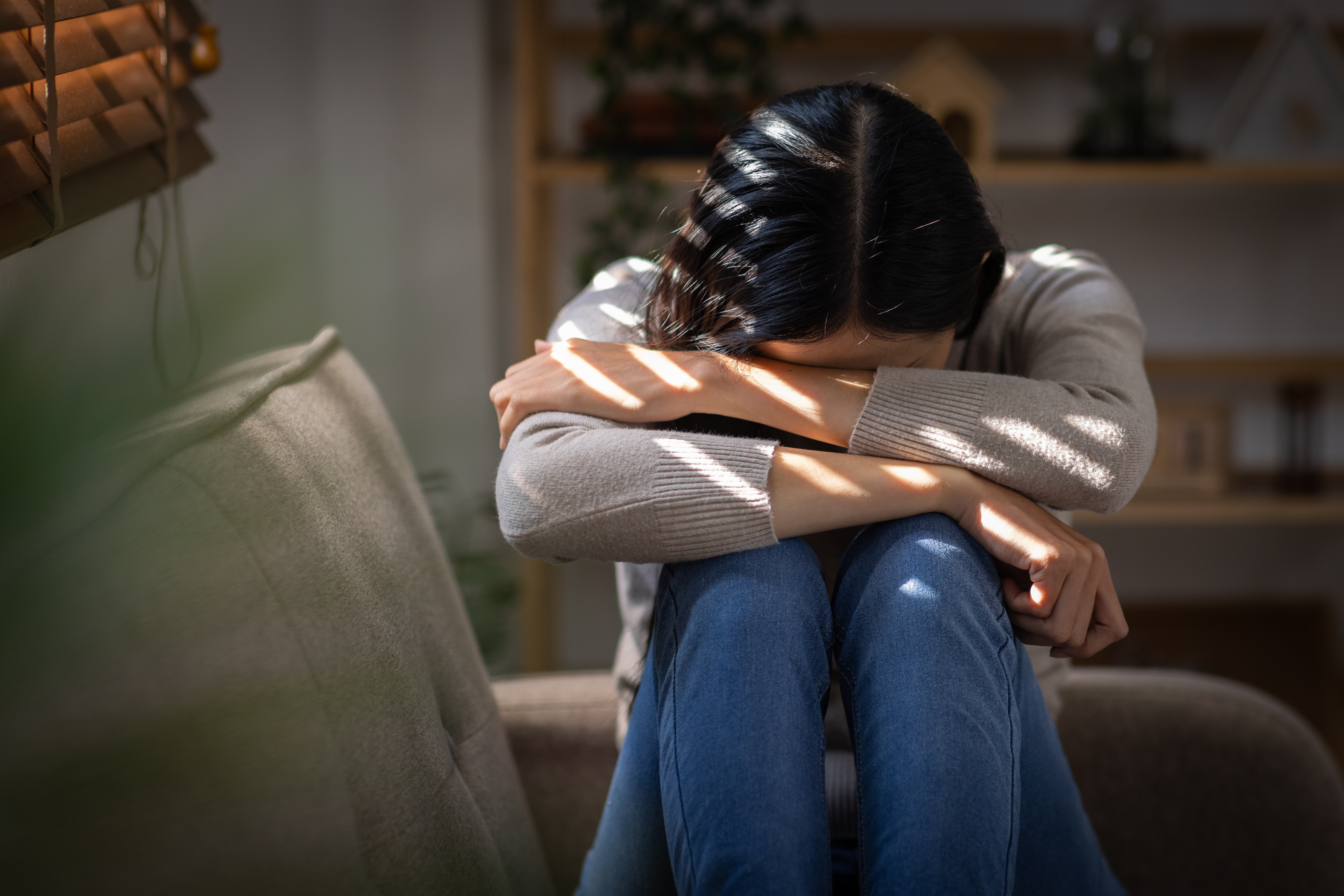 A woman is sitting on a couch with her head down for the topic relapse definition.