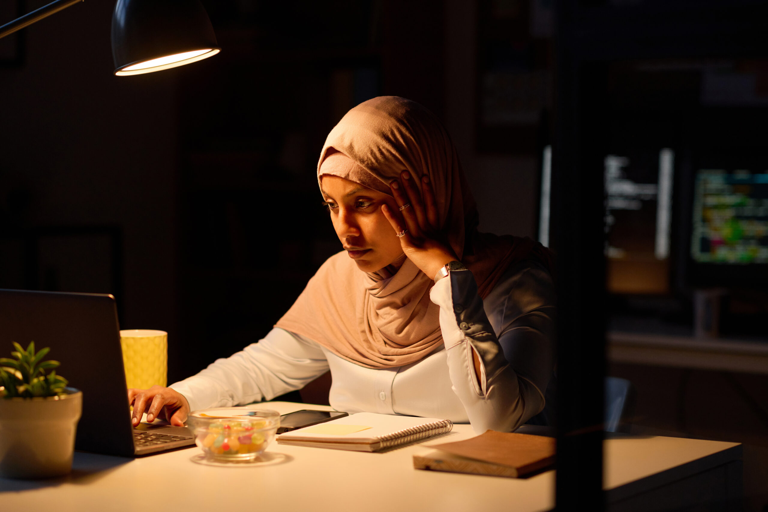 A woman working at a desk at night wondering is adderall addictive​.